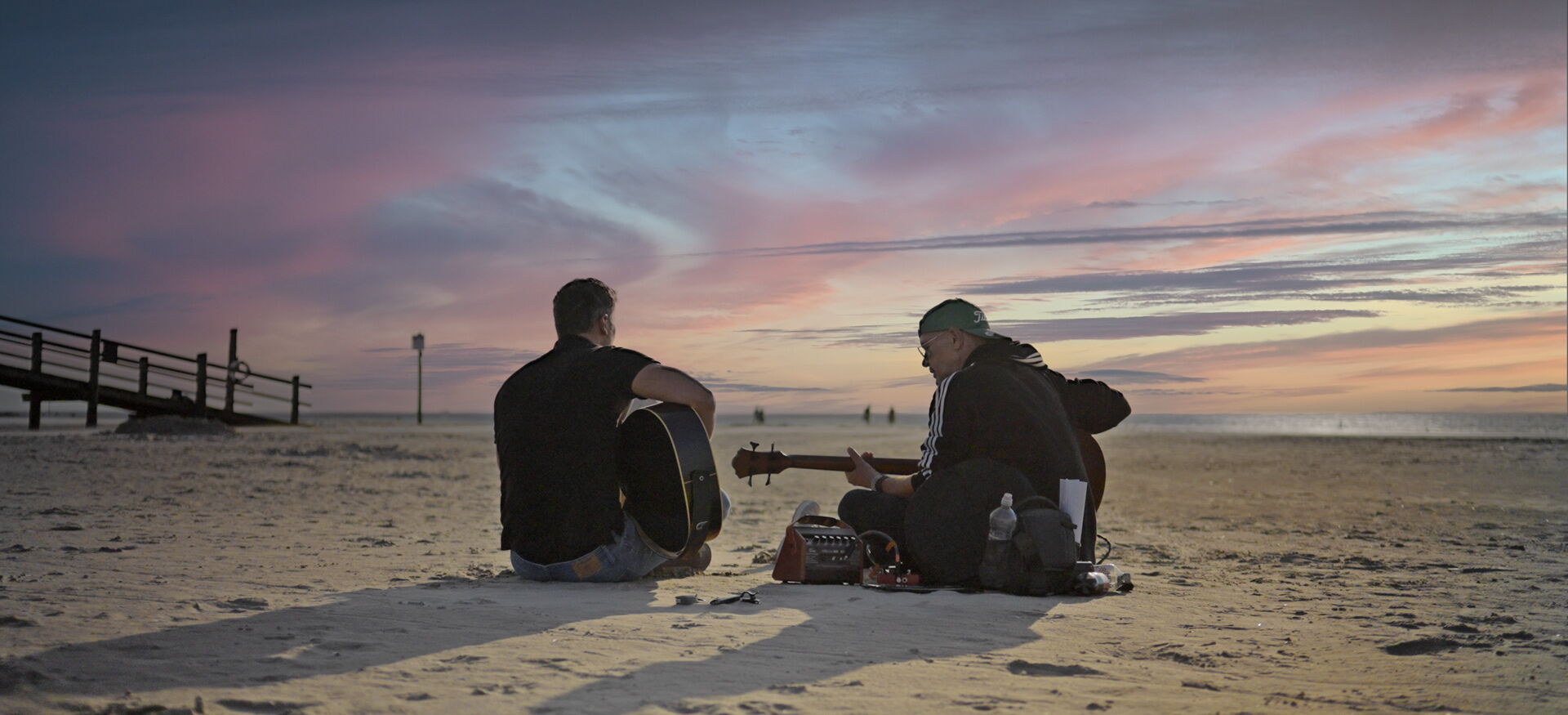 Daniel T. und ein weiterer Mann spielen Gitarre am Strand
